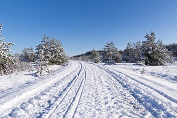 Fototapeta na wymiar Frost and snow covered road in winter forest landscape background with tire tracks