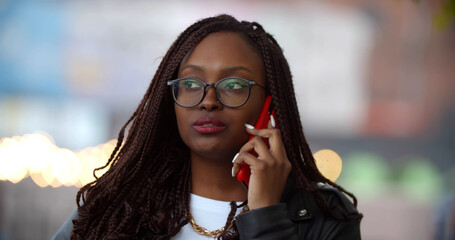 Bokeh medium shot of young afro woman outdoors on summer day speaking on cellphone