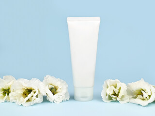 Obraz na płótnie Canvas Mockup of white squeeze bottle cosmetic cream tube for branding of medicine or cosmetics - shampoo, gel, skincare. Moisturizer blank bottle and white lisianthus flowers on blue background. Front view.