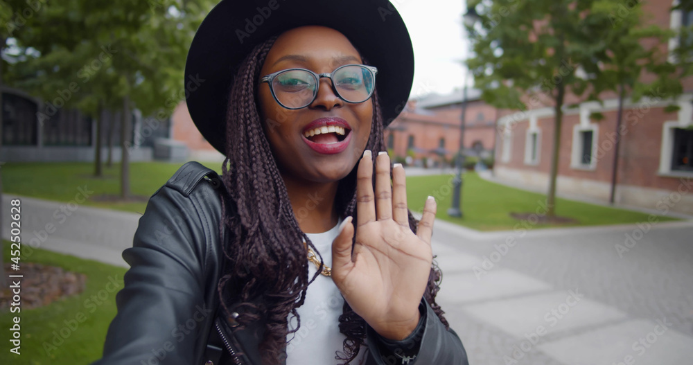 Wall mural Happy smiling african young woman making video call outdoors in city