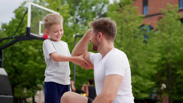 Father showing muscles to little son exercising together outdoors