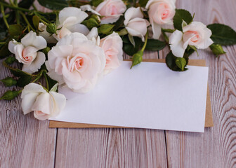 Mock up blank white paper card for text with delicate roses on a wooden background. Flat lay, top view.  Place for your text. Wedding invitation. Women's day, mother's day, birthday