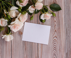 Mock up blank white paper card for text with delicate roses on a wooden background. Flat lay, top view. Place for your text. Women's day, mother's day, birthday, lovers day, celebration concept