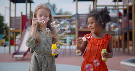 Cute diverse preschool girls blowing soap bubbles outdoors.