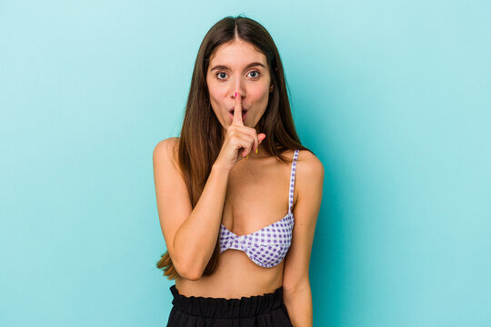Young caucasian woman wearing bikini isolated on blue background keeping a secret or asking for silence.
