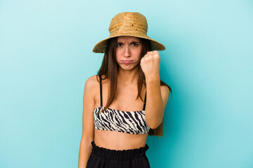Young caucasian woman going to the beach wearing bikini isolated on blue background showing fist to camera, aggressive facial expression.