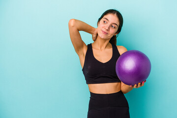 Young caucasian fitness woman holding a ball isolated on blue background touching back of head, thinking and making a choice.