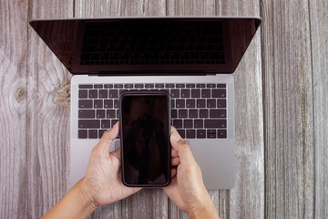Closeup mockup image of man using digital mobile phone and laptop with blank screen on wooden table.
