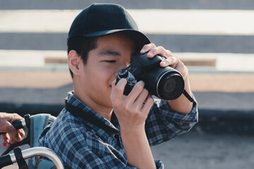 Obraz premium Disabled teenage boy son wheelchair holding a camera to take photo by himself, Activity outdoors with family on the green nature background, Diverse people concept.