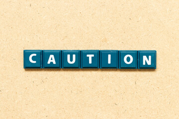 Tile alphabet letter in word caution on wood background