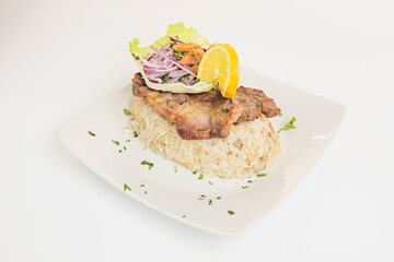Steak with white rice garnished with purple onion and lettuce with lemon on a white plate in a Peruvian restaurant