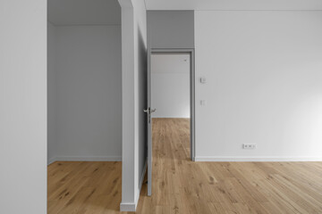 Empty minimalist modern room with white walls, opened grey door and oak wood floor