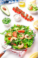 Shrimp salad with cherry tomatoes, arugula, avocado, and oil lemon dressing on white background. Top view