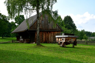 A view of a small abandoned shelter, hut, or house with an angled roof and with a dirt path leading to it with a lush garden growing on both sides seen on a cloudless summer day in Poland