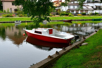 Obraz premium Close up on some ducks standing and sitting on a concrete edge or a river or lake located next to the spot where various passenger boats and other vessels are parked next to a holiday resort in Poland
