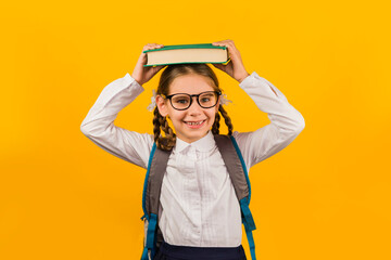 Back to school. Happy child holds a book in her head on a yellow background. Education and intellectual development of children. World book day.