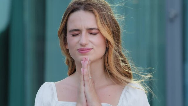 Superstitious white-skinned millennial woman believer suffer from life problems pray to god, makes gesture of apology. Religious young adult girl hold hands in prayer ask beg. Faith, religion concept
