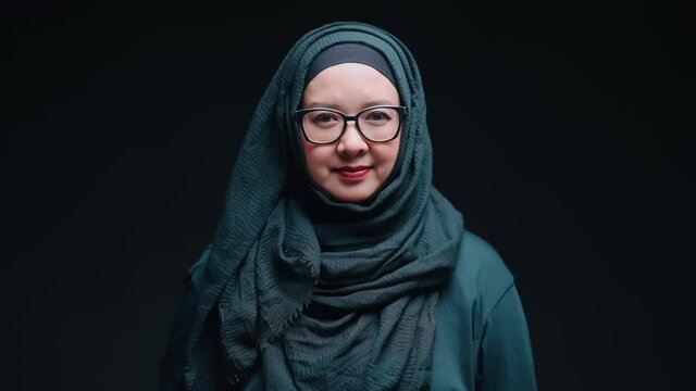 A beautiful middle-aged Asian Muslim woman. Standing smiling and raising a salam hand to greet the camera with bright cuteness
