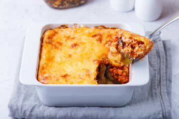 Moussaka with meat, eggplant, tomatoes, potatoes, bechamel sauce and cheese on a white plate. Traditional Greek dish. Close-up.