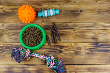 Dog toys and feed for dogs in green plastic bowl on wooden background. Top view. Dog care concept