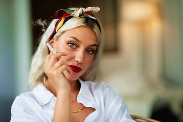 Portrait of a fashionable young woman wearing hair scarf and white shirt while smoking cigarette