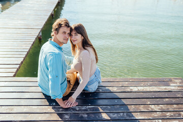 Couple of two, man and woman, sitting together on pier of wooden bridge in the sea or lake and...