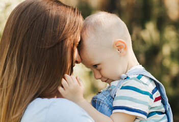 A young mother holds in her arms and hugs a little boy in the summer in nature