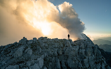 Hiker silhouette standing on rocky summit above misty valley. Nature daybreak background. Strong sun.