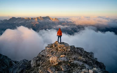 Rolgordijnen A hiker stands on the ridge watching the valley being flooded by clouds at sunset. Traveling in mountains. Adventure, Art, Travel and Hike concept. © Pavel Kašák