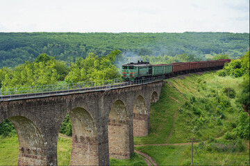 A locomotive with freight cars rides on the old viaduct