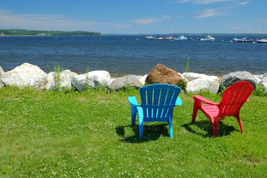 Relaxing By The Bay In Coastal New England On A Couple Of Colorful Adirondack Chairs On A Summers Day