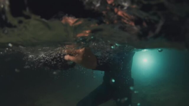 Night underwater photography. Woman in wetsuit drops the underwater camera housing in the water with splash. Splitted view above and under