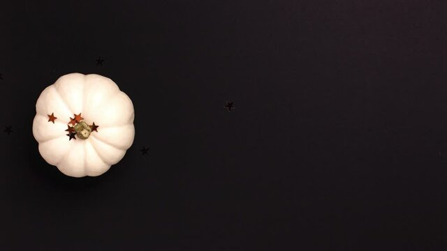 Stop motion animation of flat lay of mini decorative white pumpkin and stars on black background from above . Halloween and Thanksgiving greeting card holiday concept with copy space.