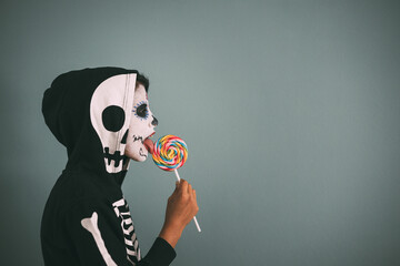 Profile portrait of girl with make-up and dead costume licking a colorful lollipop