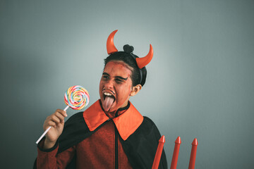 Girl in devil costume taking a bite out of a colorful lollipop