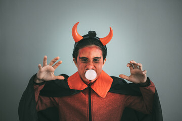 Girl in devil costume looking at the camera with hands gesturing to scare and bubble in mouth