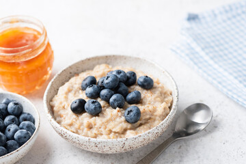 Oatmeal bowl with blueberries and honey on grey concrete table background, copy space for text. Healthy breakfast food, clean eating, dieting concept