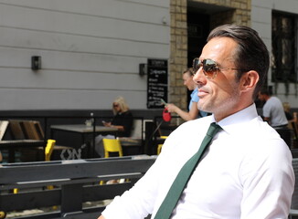 Bardzo przystojny, elegancki mężczyzna w białej koszuli i zielonym krawacie i okularach przeciwsłonecznych. - obrazy, fototapety, plakaty