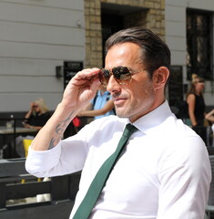Fototapeta Bardzo przystojny, elegancki mężczyzna w białej koszuli i zielonym krawacie i okularach przeciwsłonecznych. obraz