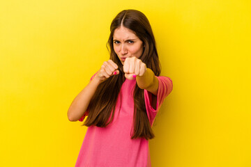 Young caucasian woman isolated on yellow background throwing a punch, anger, fighting due to an argument, boxing.