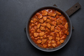 Stew turkey or chicken meat in tomato sauce. Meat dish in frying pan on black background