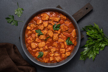 Stew turkey or chicken meat in tomato sauce. Meat dish in frying pan on black background - obrazy, fototapety, plakaty