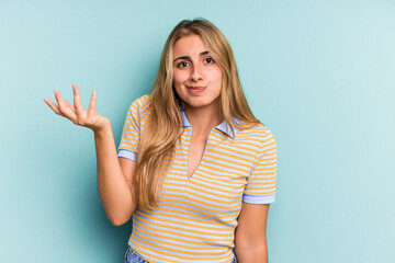 Young caucasian blonde woman isolated on blue background  doubting and shrugging shoulders in...