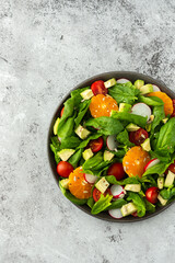 Delicious healthy salad of spinach leaves, tangerine and avocado slices, tomato and radish with seeds, salad in a plate close-up ,top view, copy space