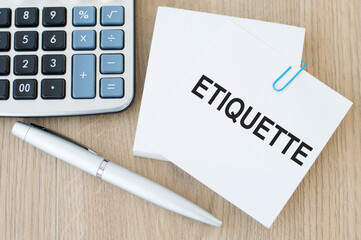 a business card with the inscription ETIQUETTE, next to a silver pen and a calculator on a wooden table. A business concept.