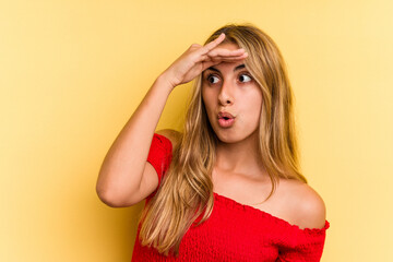 Young caucasian blonde woman isolated on yellow background  looking far away keeping hand on forehead.