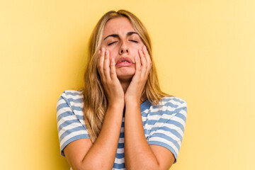 Young caucasian blonde woman isolated on yellow background  crying, unhappy with something, agony and confusion concept.