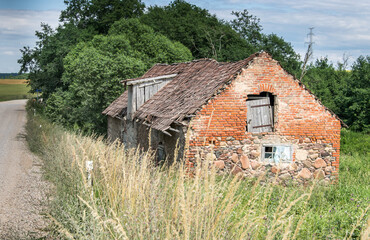 Fototapeta na wymiar Old crumbling barn with a stone and red brick tiled roof in Latvia.