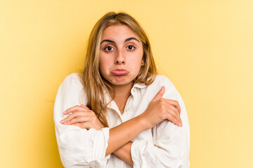 Young caucasian blonde woman isolated on yellow background  shrugs shoulders and open eyes confused.