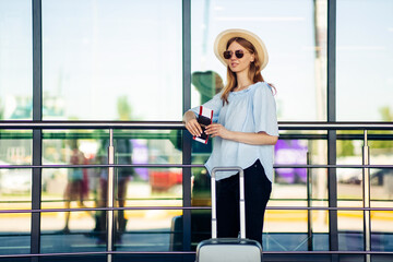 Young stylish woman traveler, with luggage at the airport, happy woman with suitcase passport and plane tickets
